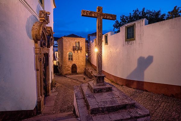Jaynes Gallery 아티스트의 Europe-Portugal-Obidos-Church and cross on cobblestone street at sunset작품입니다.